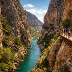 People walking on a narrow cliffside walkway above a vibrant turquoise river in a steep rocky canyon.