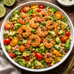 Bowl of grilled shrimp salad with avocado, cherry tomatoes, corn, and cilantro on a wooden table