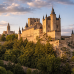 Stone medieval castle with towers atop a forested hill under a partly cloudy sunset sky