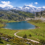 A tranquil mountain lake surrounded by green pastures with cows grazing and snow-capped peaks in the background.