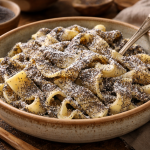 Close-up of a bowl filled with noodles covered in poppy seeds and powdered sugar.