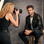 Female photographer taking a portrait of a man sitting on a stool in a photo studio
