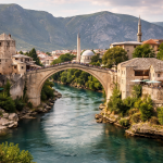 Stone arch bridge over the Neretva River with historic buildings and mountains in Mostar.