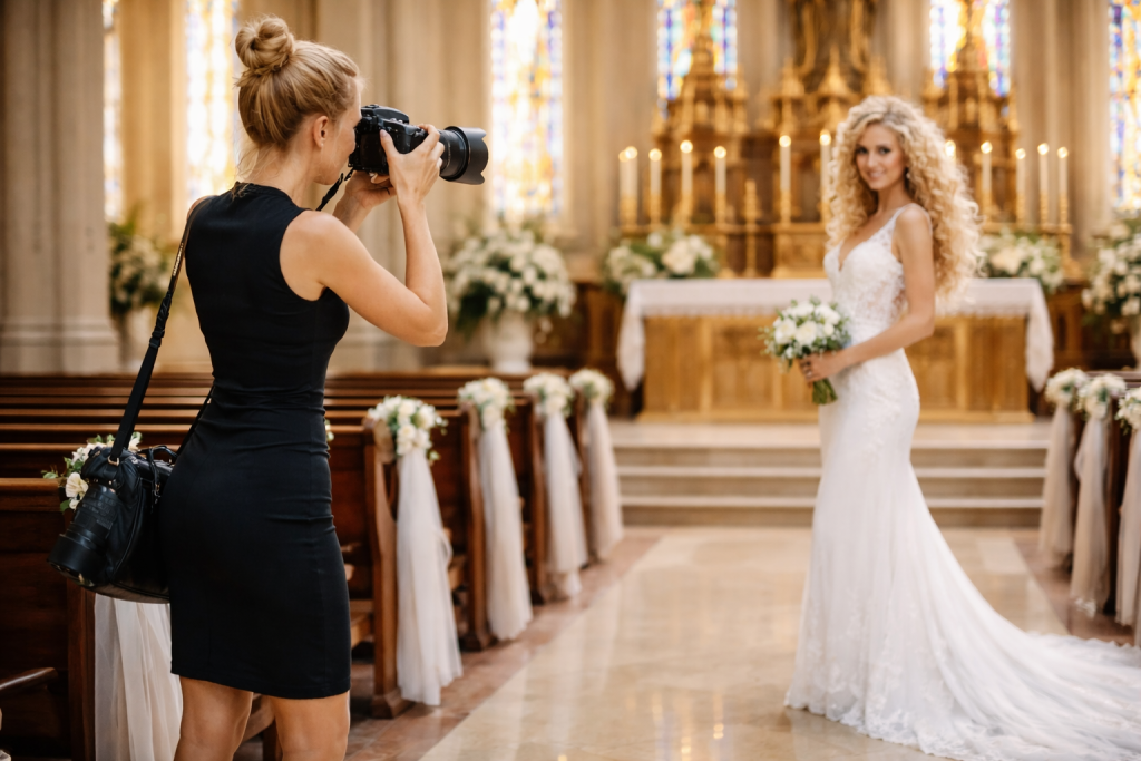 Photographer in black dress photographing bride in white gown holding bouquet inside a church